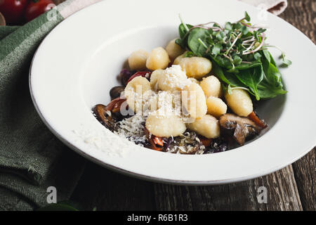 Gnocchi with roasted carrots,  red cabbage and mushrooms served in plate with fresh spinach and grated cheese, healthy vegetarian dish on rustic woode Stock Photo