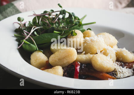 Gnocchi with roasted carrots,  red cabbage and mushrooms served in plate with fresh spinach and grated cheese, healthy vegetarian dish on rustic woode Stock Photo