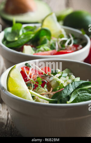 Fresh vegetables salad with avocado and quinoa, spinach, cucumber, tomato, green onion and lime on rustic wooden table Stock Photo