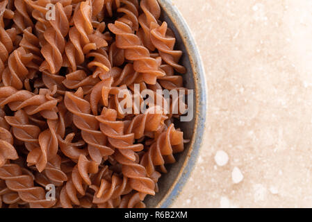 Top close view of an old stoneware bowl filled with brown rice pasta on a marble kitchen counter top. Stock Photo