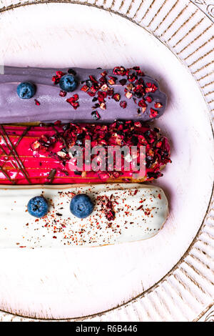 colorful eclairs red white violet with blueberry, raspberry, isolated on white background Stock Photo