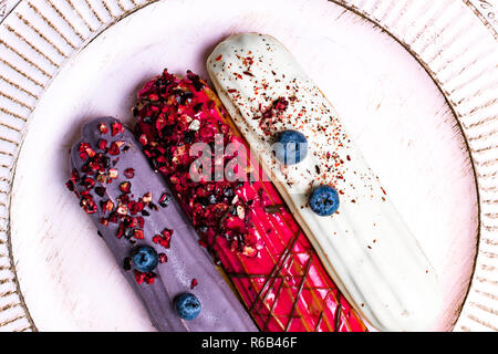 colorful eclairs red white violet with blueberry, raspberry, isolated on white background Stock Photo