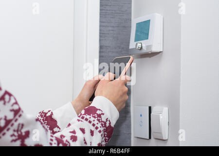 Girl adjusts and regulate the room temperature with smart phone on switch wall. Smart WiFi light switch and temperature regulator. Smart house concept Stock Photo