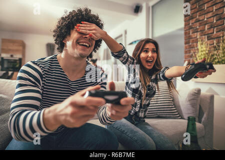 Excited couple is playing video games at home sitting on sofa. They have great weekend in nice company indoors. Stock Photo