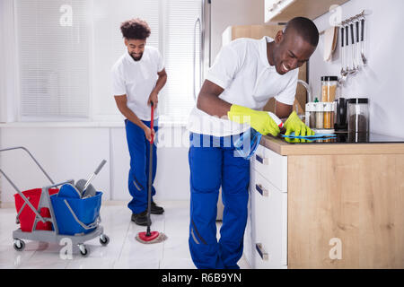 Smiling Two Young Male Janitor Cleaning The Kitchen Stock Photo