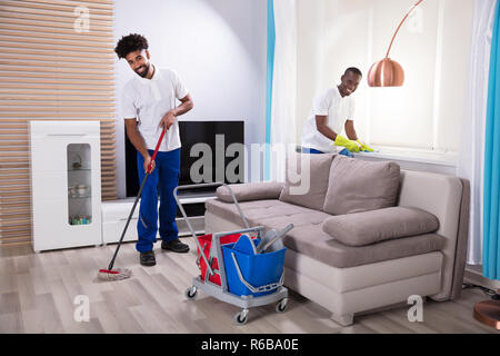 Smiling Two Young Male Janitor Cleaning The Living Room Stock Photo