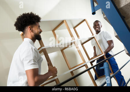 Two Male Movers Carrying The Empty Shelf At Home Stock Photo