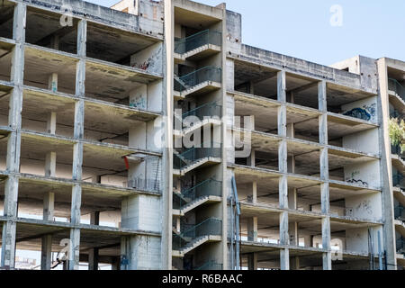 Huge multi floors concrete structure of abandoned building with stairs surrounded by grass and trees with blue sky in the background. Architecture det Stock Photo