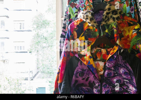 Handmade colorful jackets hanged near a window with day light entering from outside. Buildings of the street can be seeing in the background. No peopl Stock Photo