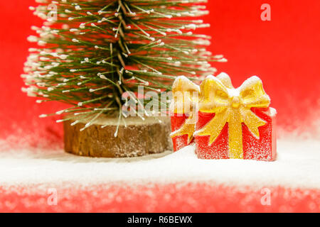 Two gift boxes and Christmas tree covered with snow on a red background, close up Stock Photo