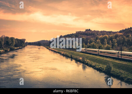 High-speed train on the bank of a river in evening sunset Stock Photo