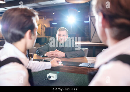Content handsome young businessman in formal jacket sitting at bar counter and making order while talking to bartender in pub Stock Photo