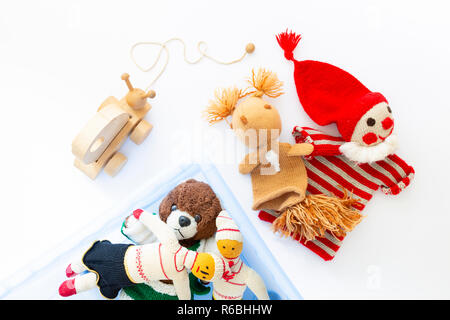 Top view of cute and funny vintage children toys in and besides a blue plastic box on white background. Assortment consists of a clown, a squirrel, a  Stock Photo