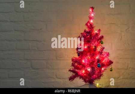 lighted and decorated christmas tree isolated on a white brick wall background Stock Photo