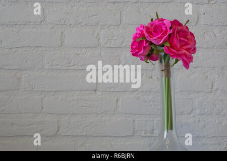 glass vase with pink roses isolated on a white brick wall, romantic valentines day background Stock Photo