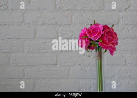 pink roses in a glass vase isolated on a white brick wall background, romantic valentines day or interior background Stock Photo