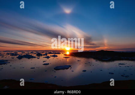 Sunset over Disko Bay in Greenland with circular halo effect. Halo is the name for a family of optical phenomena produced by sunlight Stock Photo
