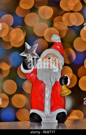 Santa holding the North Star  in one hand and a bell in the other, against a backdrop of soft bokeh Christmas tree lights. Stock Photo