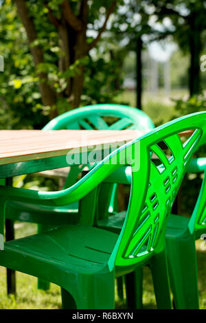Plastic outdoor furniture in the sun. Green chairs lit by the sun on the lawn Stock Photo