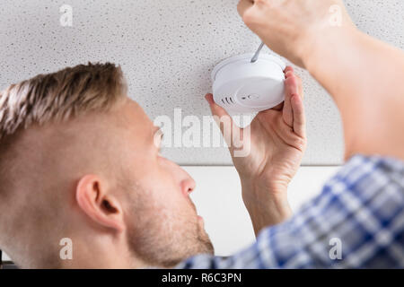 Person's Hand Using Screwdriver To Install Smoke Detector Stock Photo
