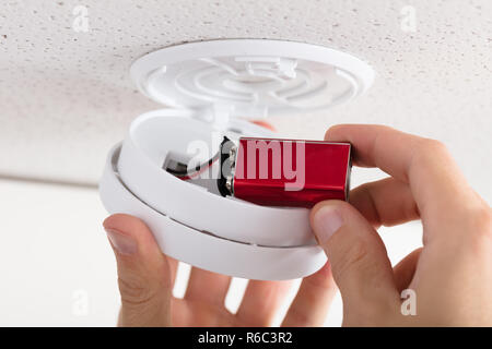 Person's Hand Inserting Battery In Smoke Detector Stock Photo