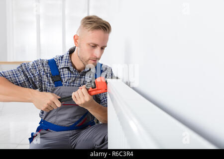 Male Plumber Fixing Thermostat Using Wrench Stock Photo