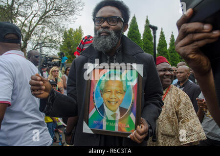 A man holds a picture of Nelson Mandela and a South African flag as thousands paid tribute to the former South African president, outside his home in Houghton, Johannesburg, South Africa, on December 9, 2013. Scores of people gathered at the site over the weekend. The elder statesman died Thursday, December 5, 2013. PHOTO: EVA-LOTTA JANSSON Stock Photo