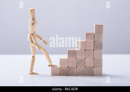 Side View Of A Wooden Figure Climbing Staircase Stock Photo