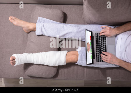 Man With Plastered Leg Using Laptop Stock Photo