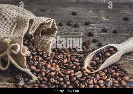 Roasted Coffee Beans Spilled out of Burlap Sack on Wooden Background. Copy Space for Text. Stock Photo
