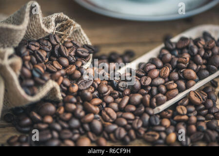 Roasted Coffee Beans Spilled out of Burlap Sack on Wooden Background Stock Photo