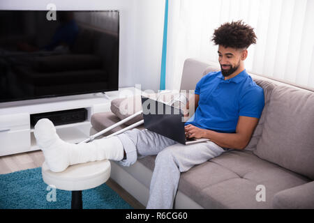 Man With Broken Leg Using Laptop Stock Photo