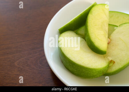 Close view of green sliced apples on a white plate atop a brown wood table. Stock Photo