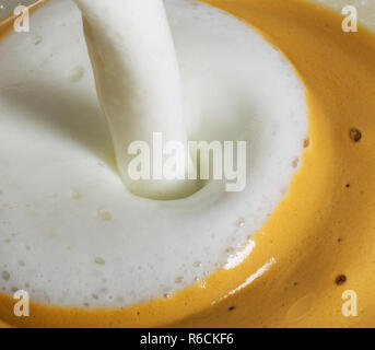 Frothy hot milk being poured into cup of coffee Stock Photo