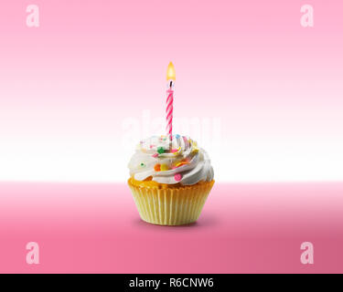 Birthday cupcake with frosting and a lit candle on a pink surface Stock Photo