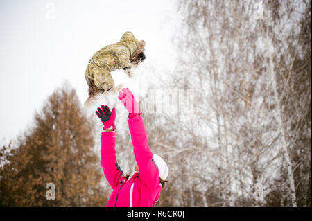 dog throws up into the sky. Walk in the winter outdoors with a dog breed Shih Tzu. A woman in a bright red warm ski clothing walking in the snow with your pet, a little shih tzu dressed in overalls. care for animals, and loves playing with the dog Stock Photo