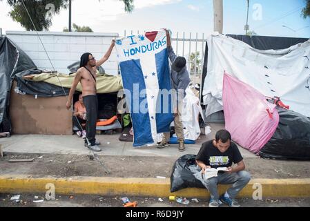 Tijuana, Mexico. 04th Dec, 2018. Migrants are holding a Honduran flag in front of the Benito Juarez sports complex, which was closed due to flooding. Currently more than 6000 migrants from Central America are waiting in the border town of Mexican Tijuana to apply for asylum in the USA. As only a limited number of cases are processed at the San Ysidro border crossing, there are months of waiting time. Credit: Bruno Gallardo/dpa/Alamy Live News Stock Photo