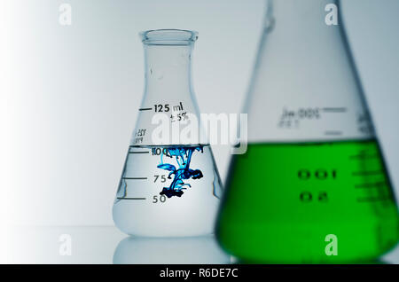 Two conical flasks containing green and blue liquids, focus on background. Stock Photo