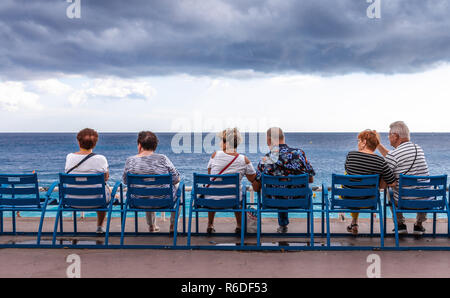 Nice, France - October 1, 2018: People relaxing on public bench and looking to sea view at Mediterranean sea of Nice, France on cloudy day. Stock Photo