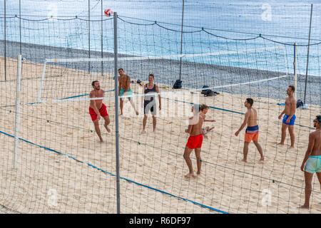 Nice, France - October 1, 2018: Group of men playing volleyball inside sand court at Mediterranean beach of Nice, France. Stock Photo