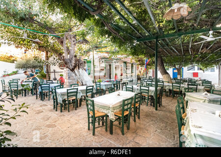 Hydra, Greece - October 4th, 2018: A traditional greek taverna with wooden green chairs in the city center, Hydra, Greece. Stock Photo
