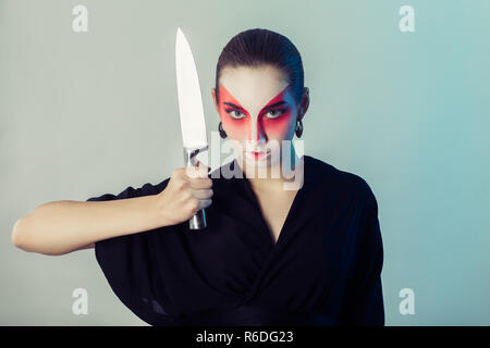 serious woman, professional geisha makeup, in black kimono with big kitchen knife looking at camera Stock Photo