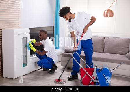 Smiling Two Young Male Janitor Cleaning The Living Room Stock Photo