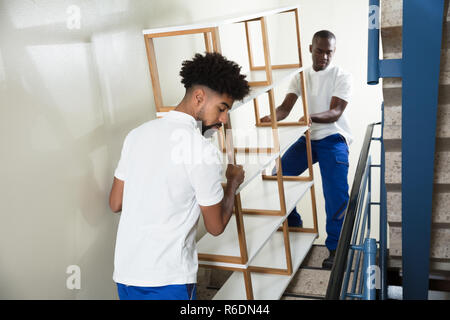 Two Male Movers Carrying The Empty Shelf At Home Stock Photo