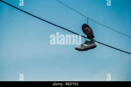 Shoes hanging on cables as spot sign of drug dealing with blue sky background Stock Photo