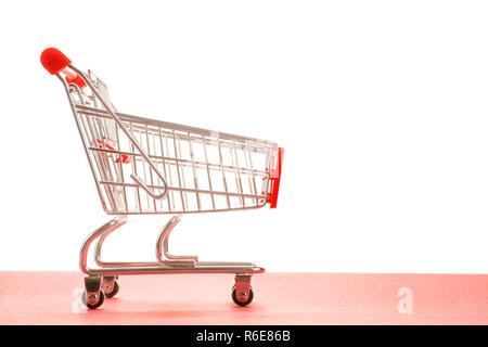Small empty shopping cart with red handle side view. On red and white background with copy space Stock Photo