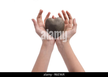 Young girl hands holding a heart made out of clay. Conceptual image with hands and heart isolated on white background. Symbol for love. Stock Photo
