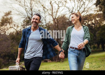 Happy couple walking in the park holding hand and carrying picnic basket. Loving couple going on a picnic at the park.