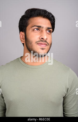 Portrait of young handsome Indian man thinking against gray background Stock Photo