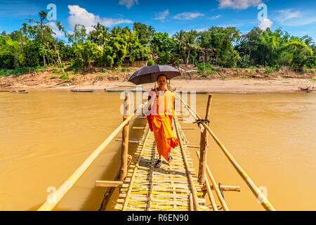 A Young Buddhist Monk Walks Across A Bamboo Bridge Over Nam Khan In Luang Prabang Laos